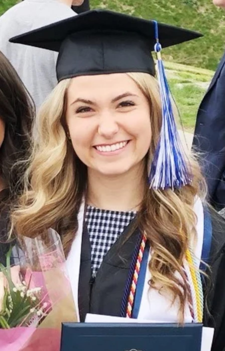 Ryan Kelly at college graduation, wearing a cap and gown and holding flowers and a diploma cover